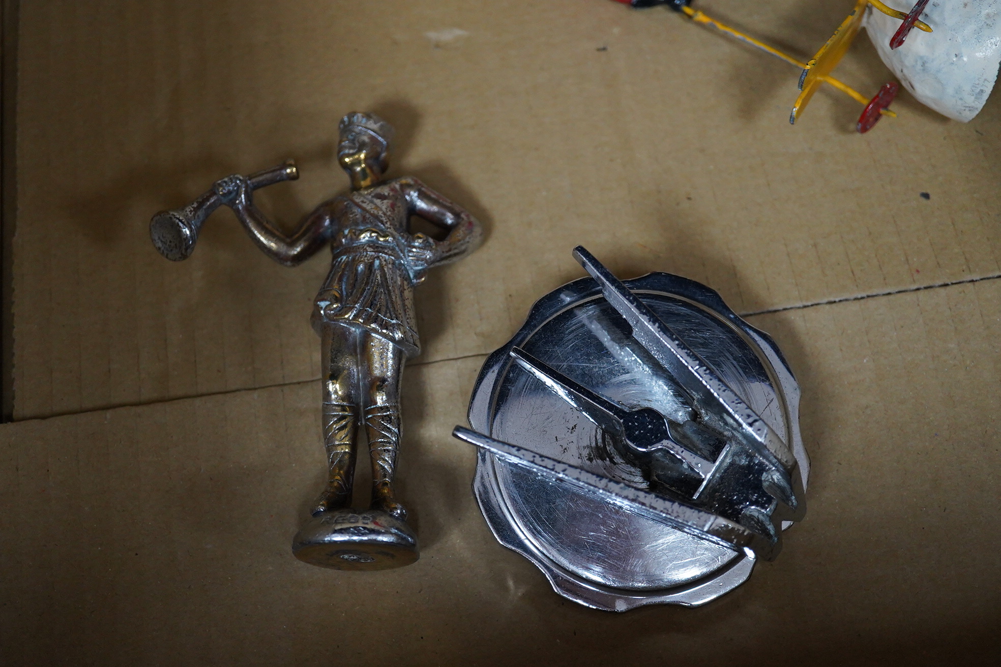 Six car mascots including five chrome and brass examples; a female figure, a cherub with harp, an Art Deco winged figure, etc. and a cold painted spelter figure of a skier